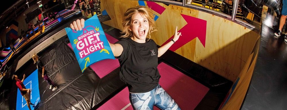 Girl jumping on a trampoline at bounce holding a gift of flight gift pack